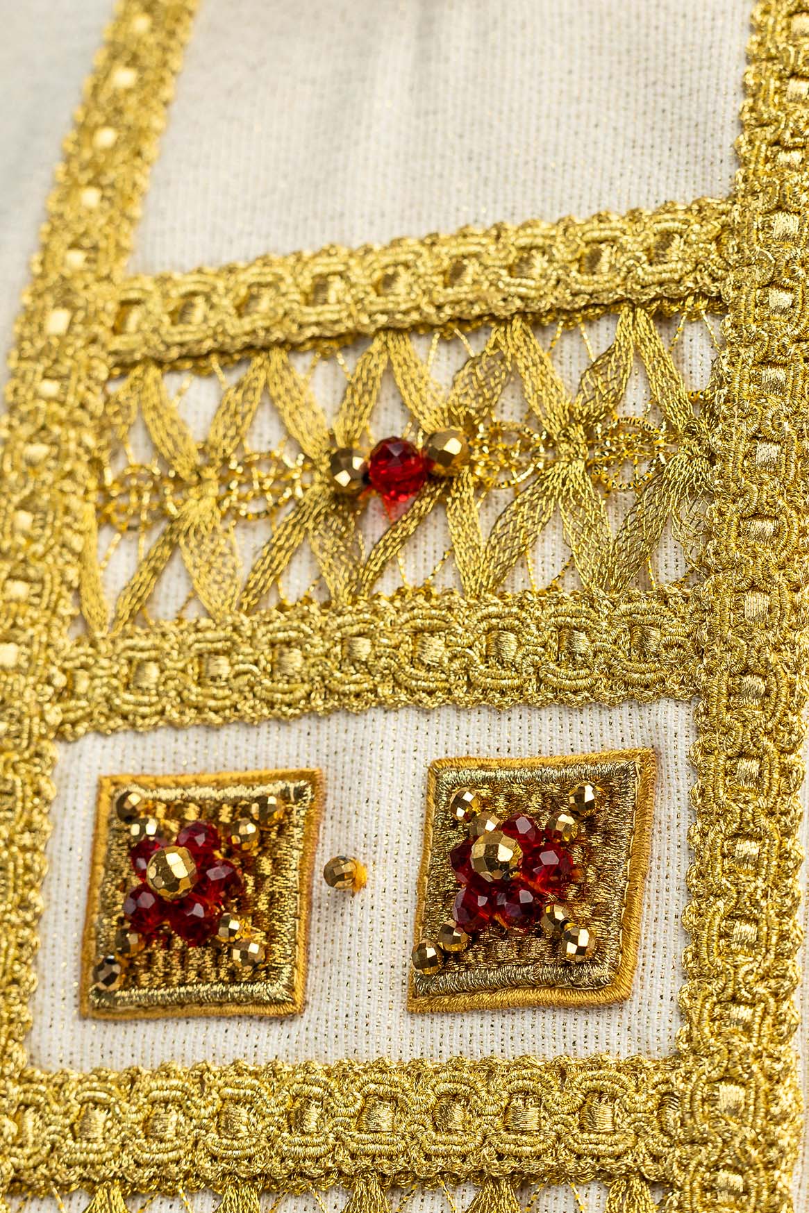Casula avorio, close-up del ricamo dorato traforato con pietra rossa